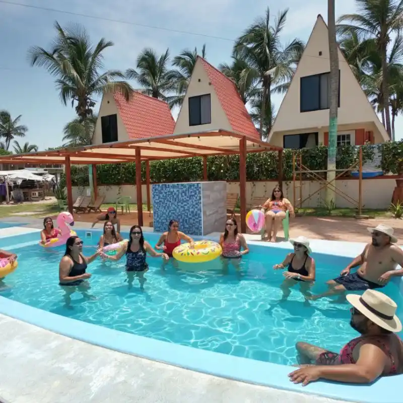 Grupo grande de personas disfrutando de la alberca exclusiva para huéspedes frente a las cabañas alpinas privadas en Mar de Plata, Tuxpan.