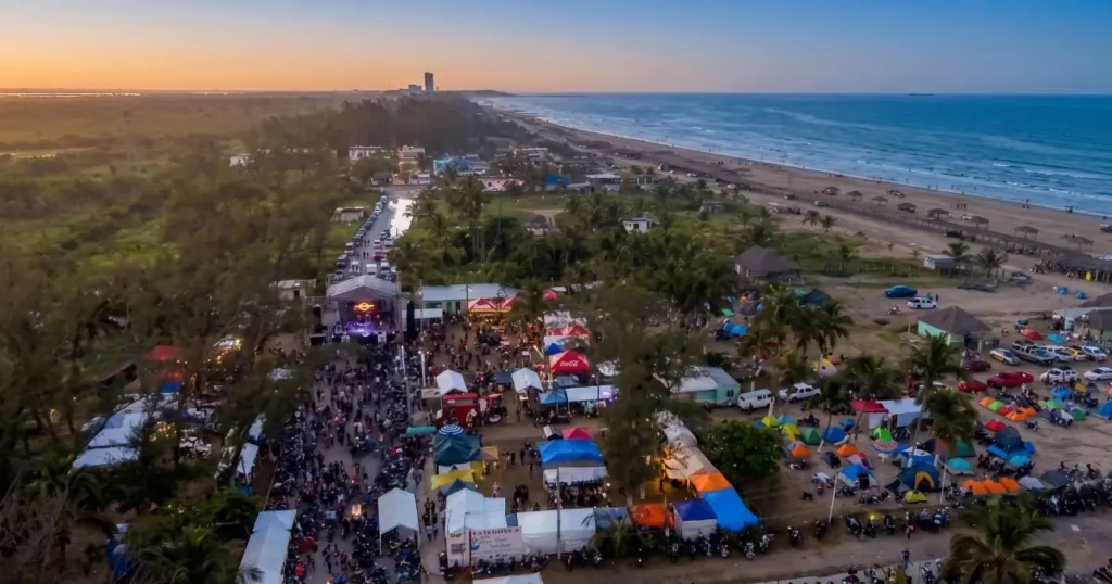 Vista aérea de un gran evento en la playa Mar de Plata en Tuxpan con escenario, carpas y multitud al atardecer.