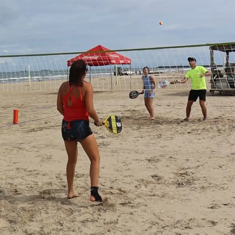 Grupo de personas jugando un partido de tenis playero mixto en la arena de la playa Mar de Plata en Tuxpan, con un jugador golpeando la pelota sobre la red