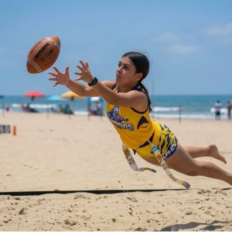 Jugadora de tocho bandera femenil lanzándose por el aire para atrapar un balón de fútbol americano sobre la arena en la playa Mar de Plata, Tuxpan.