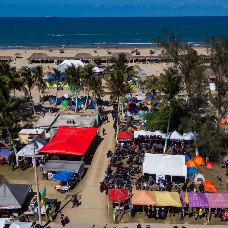 Vista aérea de un Motofest en la playa Mar de Plata, Tuxpan, mostrando decenas de motocicletas estacionadas, stands comerciales y una gran zona de campamento con tiendas de campaña bajo las palmeras.