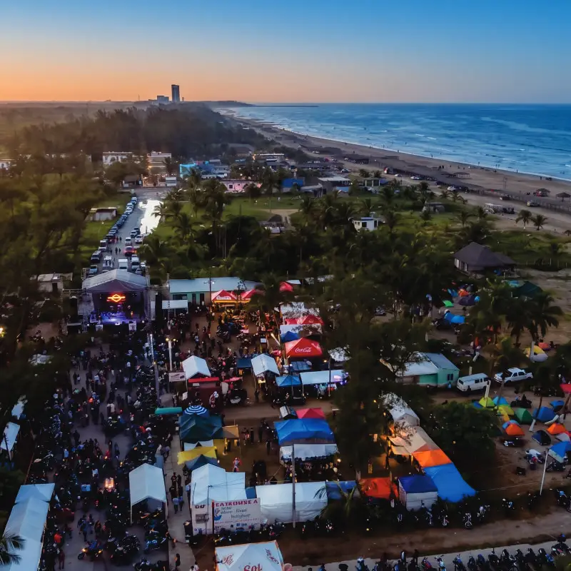 Vista aérea panorámica de un gran festival masivo al atardecer en las instalaciones del club Mar de Plata Tuxpan, mostrando escenario, carpas, asistentes y la playa al fondo.